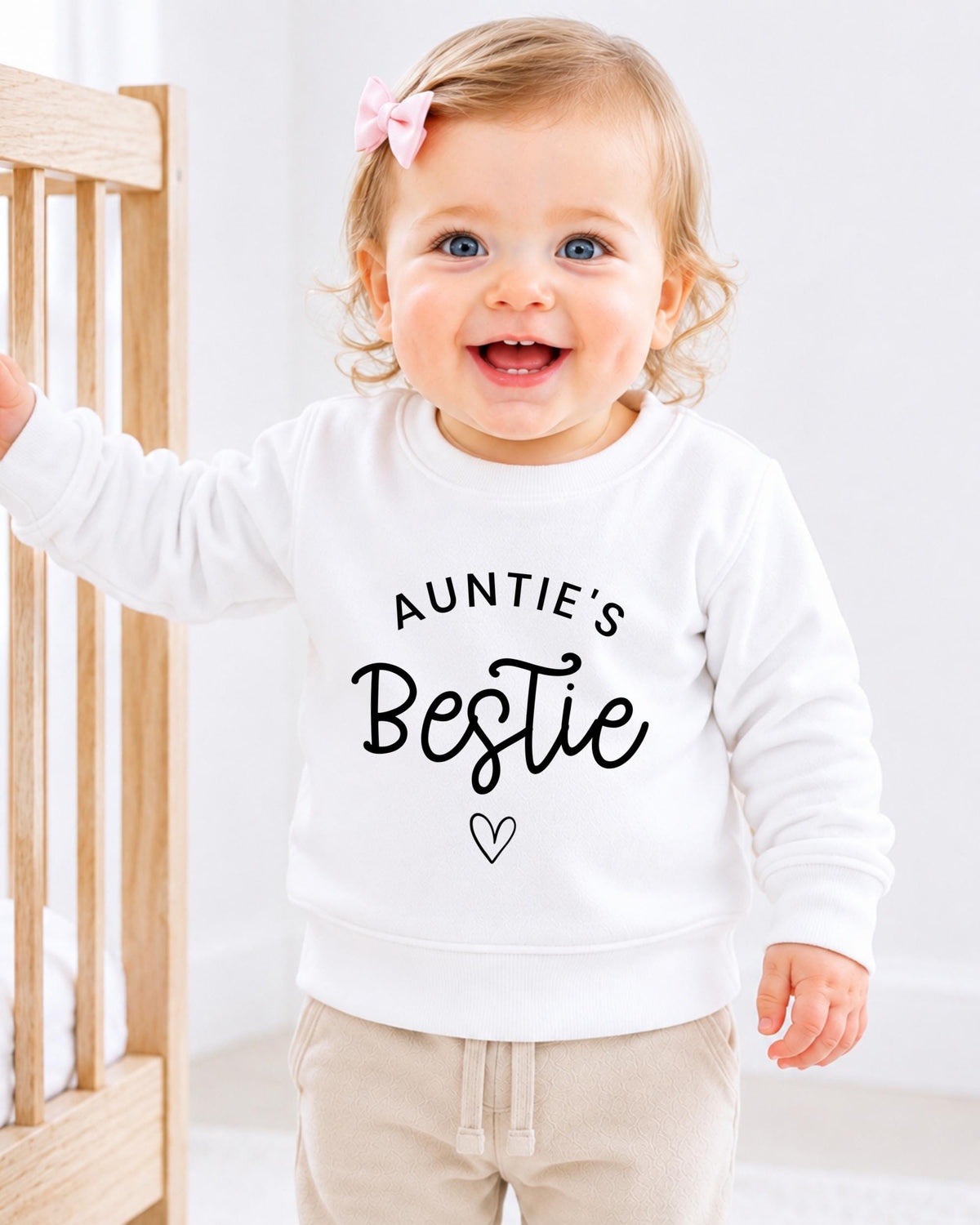 A smiling baby girl wearing a white sweatshirt with the text "Auntie's Bestie" printed on it.