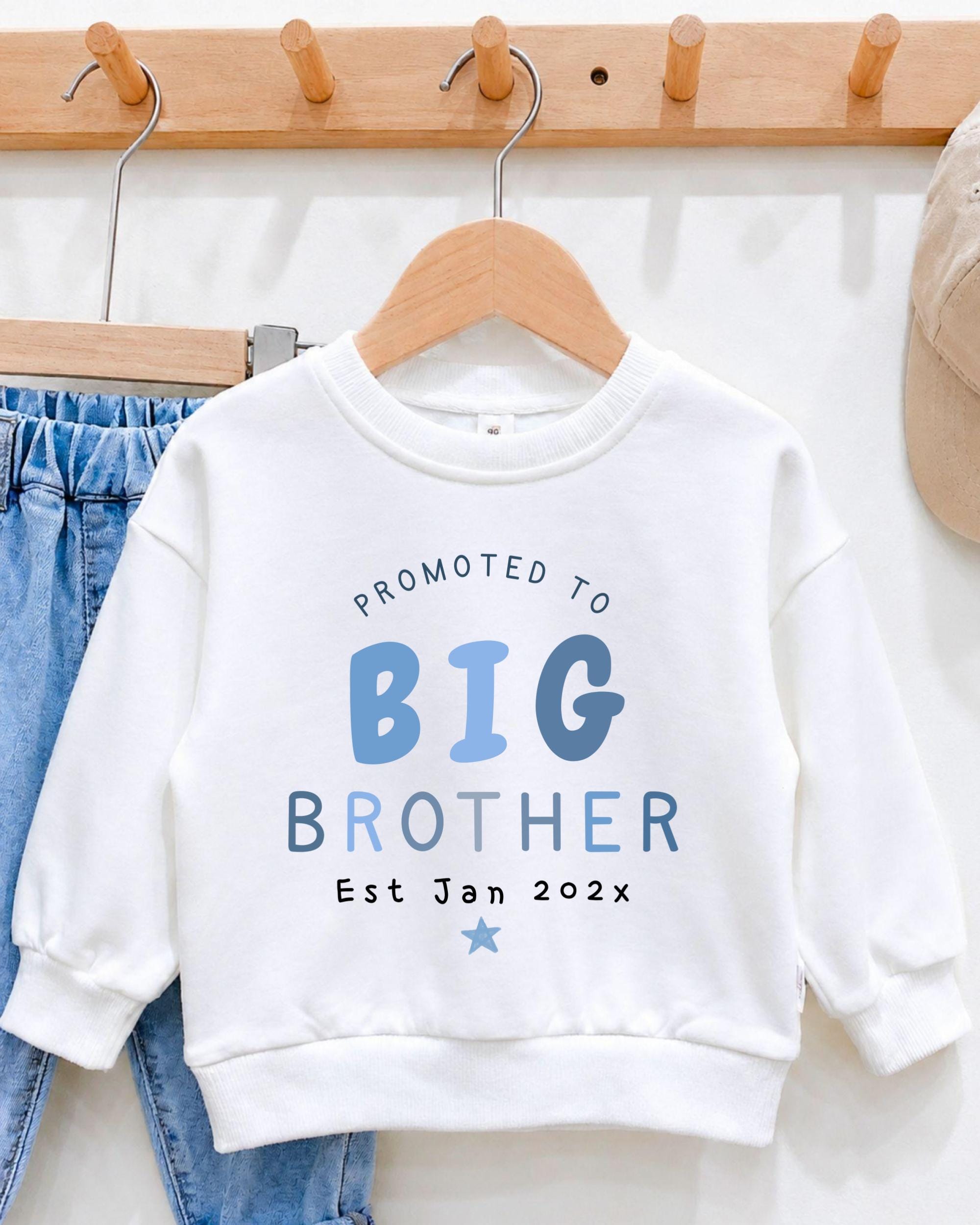 A white sweatshirt with text printed on it, hanging on a wooden hanger.