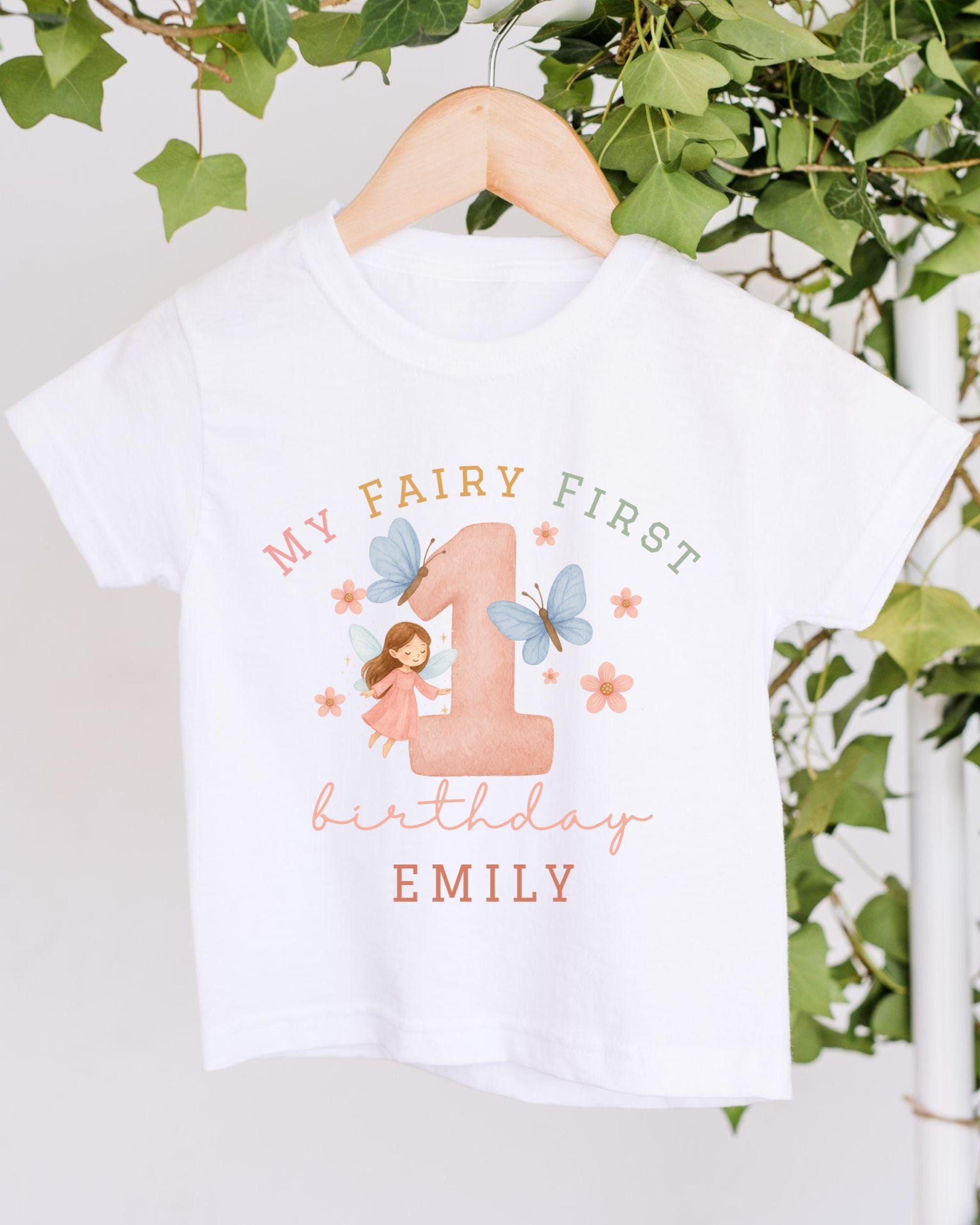 A white t-shirt with a graphic design featuring a fairy and the number 1, along with the text "My Fairy First birthday Emily".