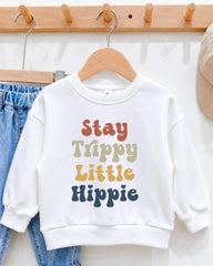 A white sweatshirt with colorful text printed on it, hanging on a wooden hanger.