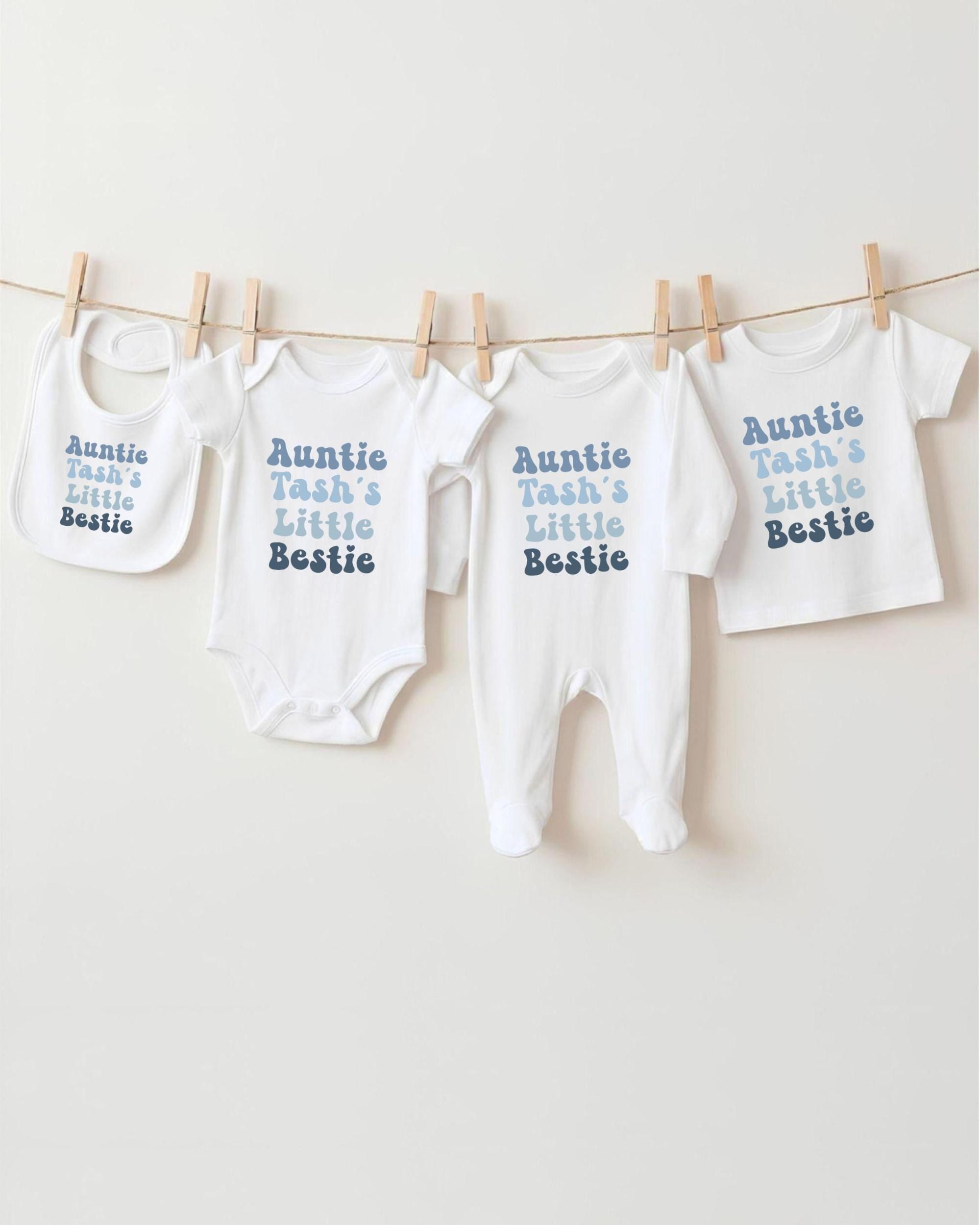A row of white baby clothes with the text "Auntie Tash's Little Bestie" printed on them, hanging on a clothesline.