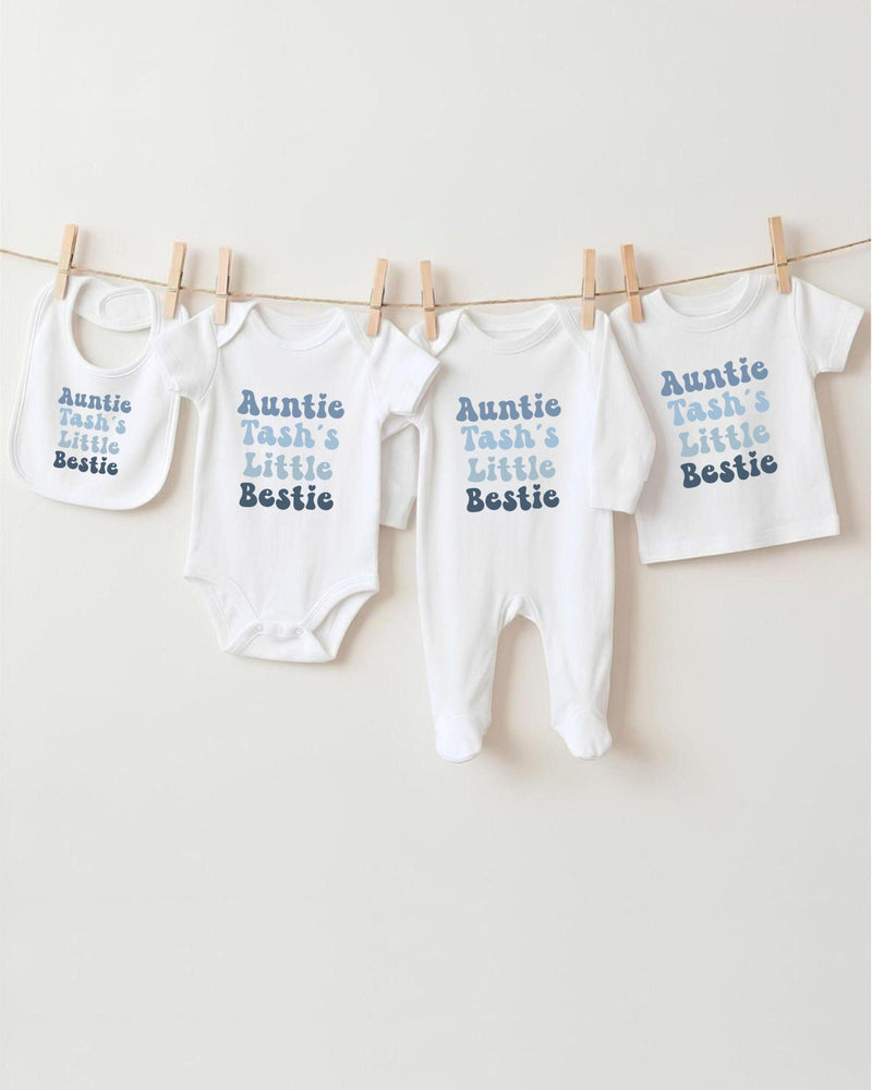 A row of white baby clothes with the text "Auntie Tash's Little Bestie" printed on them, hanging on a clothesline.