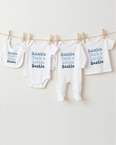 A row of white baby clothes with the text "Auntie Tash's Little Bestie" printed on them, hanging on a clothesline.