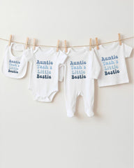 A row of white baby clothes with the text "Auntie Tash's Little Bestie" printed on them, hanging on a clothesline.