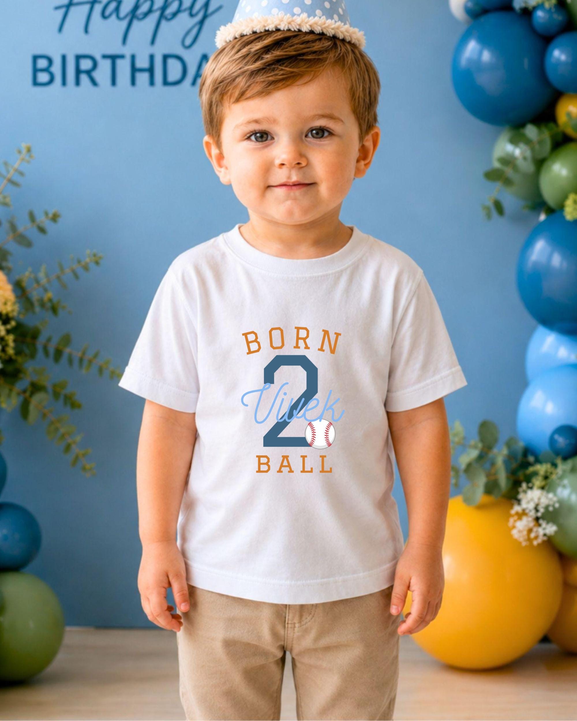 A young boy wearing a white t-shirt with the text "BORN 2 VIRK BALL" stands in front of a blue birthday backdrop with balloons.