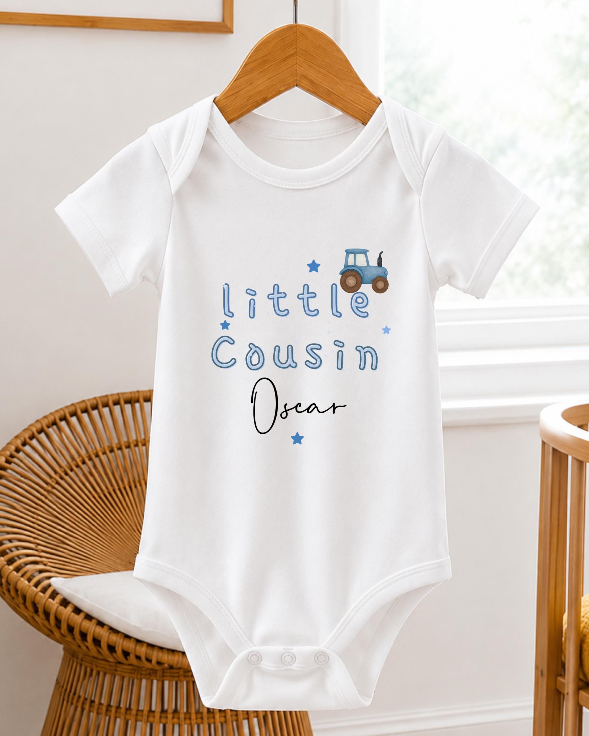 A white baby onesie with blue text and a tractor graphic, hanging on a wooden hanger.