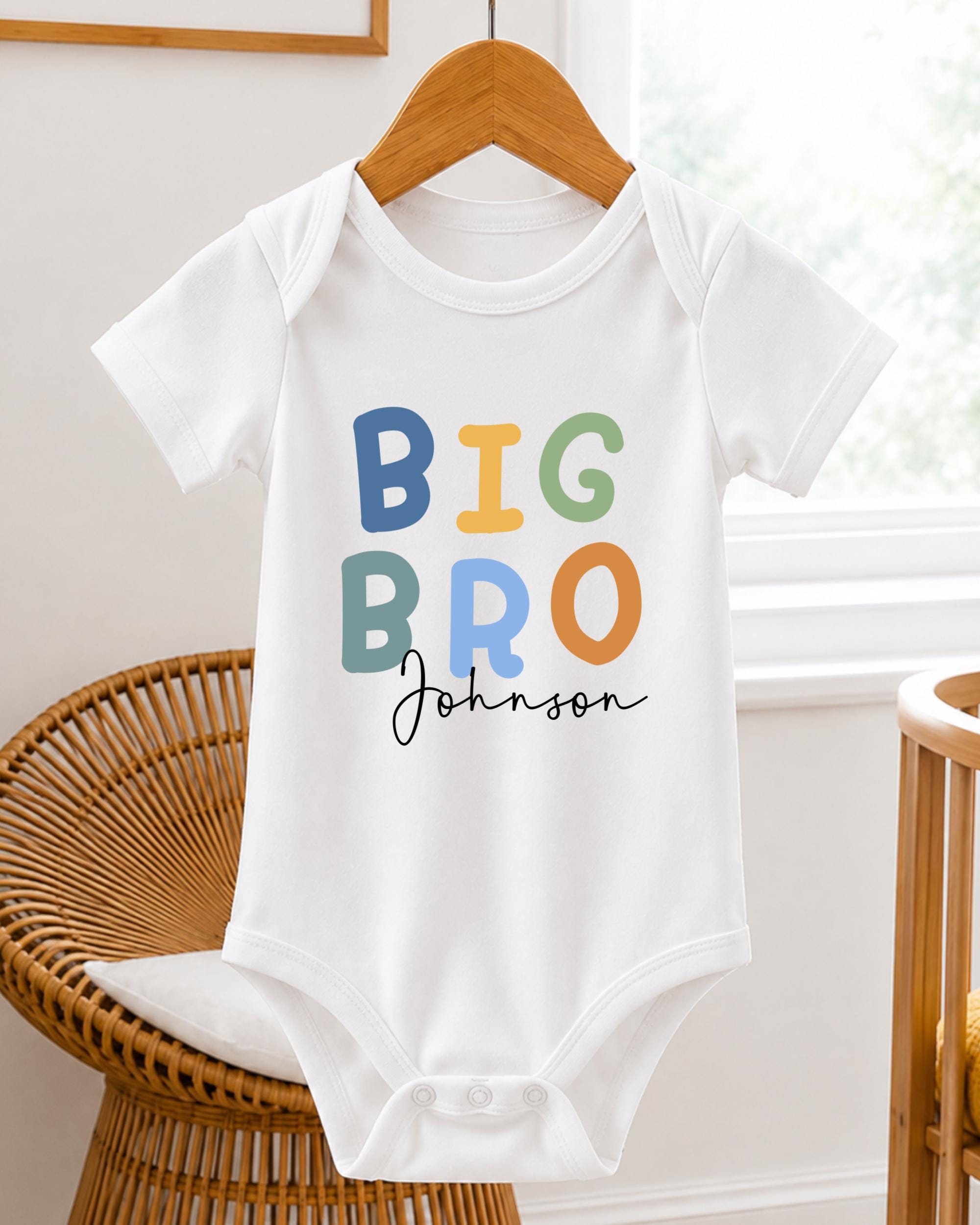 A white baby onesie with the text "BIG BRO Johnson" printed on it, hanging on a wooden hanger.