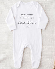A white onesie with the text "Your Bestie Is Growing a Little Bestie" printed on it.