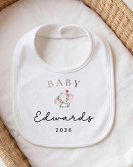 A white baby bib with a personalized text and an image of an elephant.