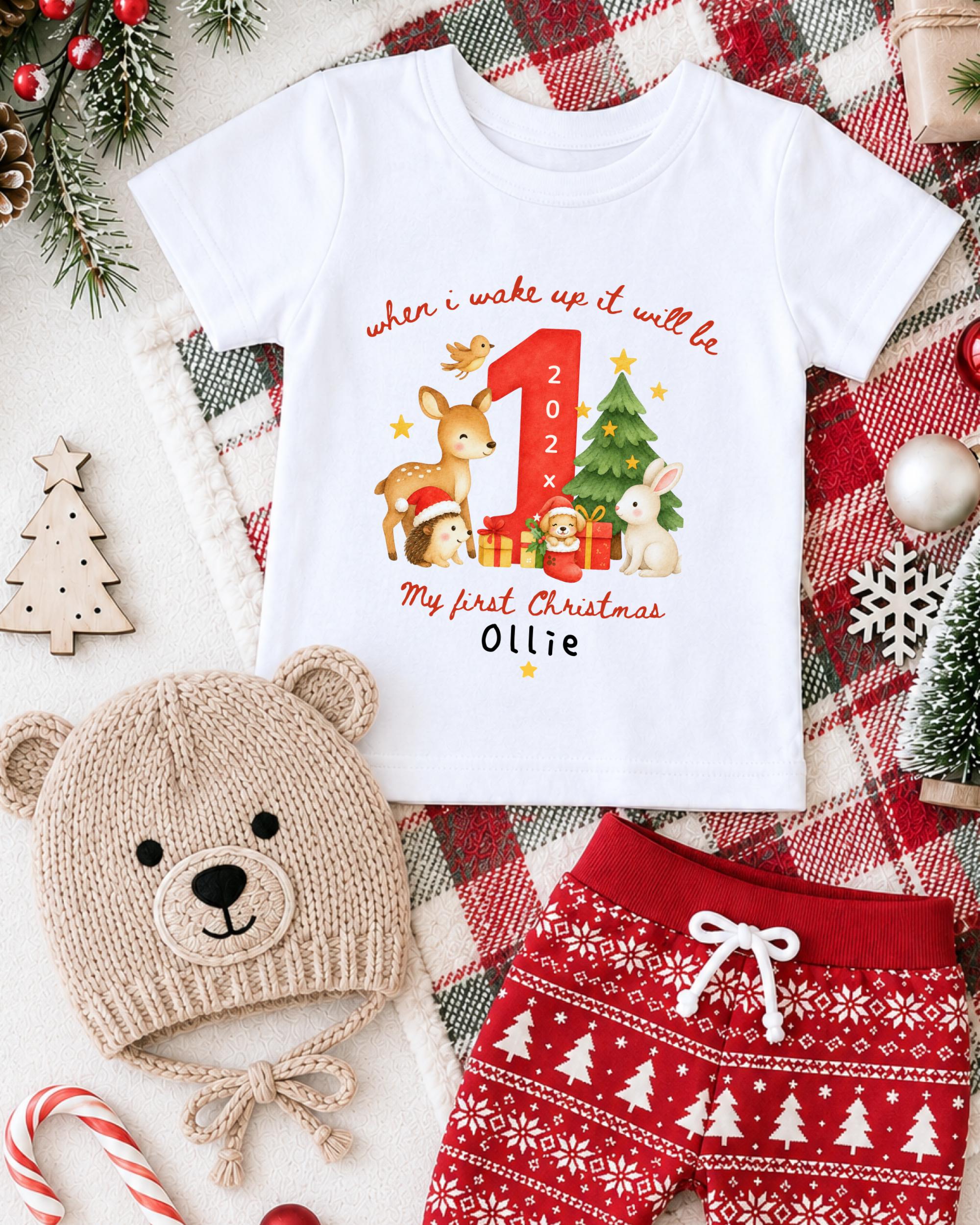 A white t-shirt with a Christmas-themed design, a beige knit hat, red shorts, and other holiday decorations are arranged on a plaid blanket.