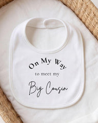 A white bib with the text "On My Way to meet my Big Cousin" printed on it.