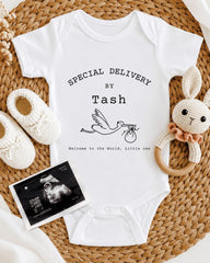 A white baby onesie with text, a crocheted bunny toy, and a baby bootie, all arranged on a woven placemat.