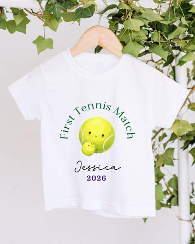 A white t-shirt with a tennis ball design and text printed on it, hanging on a wooden hanger.