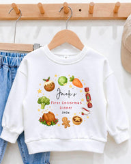 A white sweatshirt with a personalized Christmas dinner design printed on it, hanging on a wooden hanger.