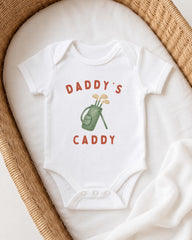 A white onesie with the text "DADDY'S CADDY" printed on it, along with an illustration of a golf club.