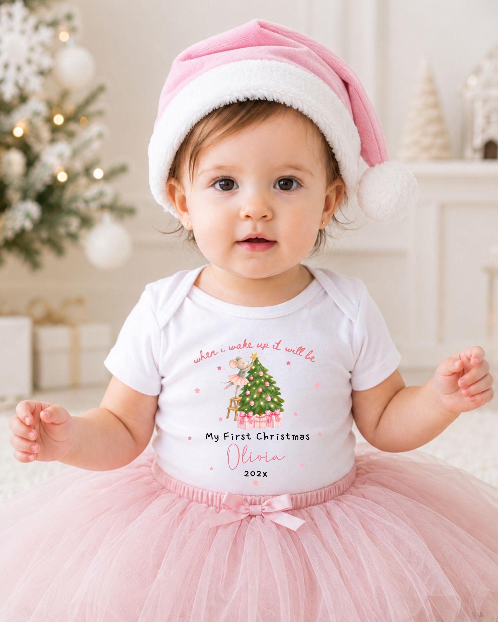 A young girl wearing a pink hat and a white t-shirt with a Christmas tree design, posing in front of a Christmas tree.