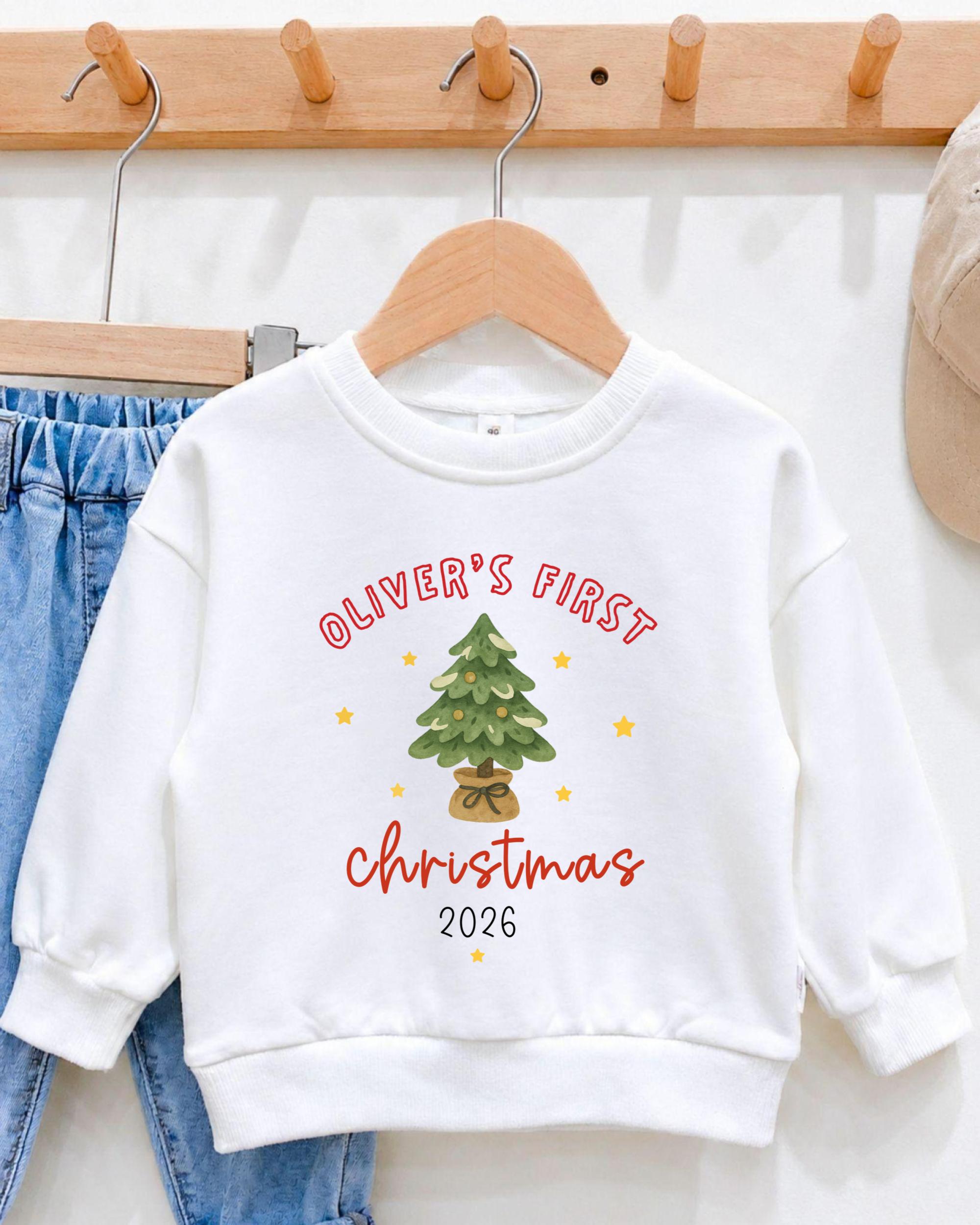 A white sweatshirt with a Christmas tree design and text printed on it, hanging on a wooden hanger.