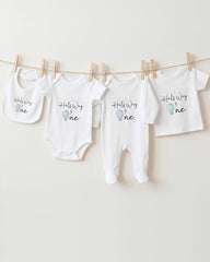 A row of four white baby clothes, including onesies and bibs, hanging on a clothesline.