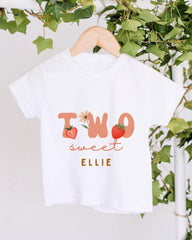 A white t-shirt with the text "TWO sweet Ellie" printed on it, along with illustrations of strawberries and leaves.