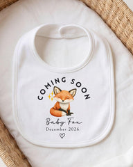A white bib with a graphic of a sleeping fox and text that says "Coming Soon Baby Fox December 2026".