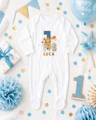 A white onesie with the number 1 and a cartoon animal printed on it, surrounded by birthday decorations and confetti.