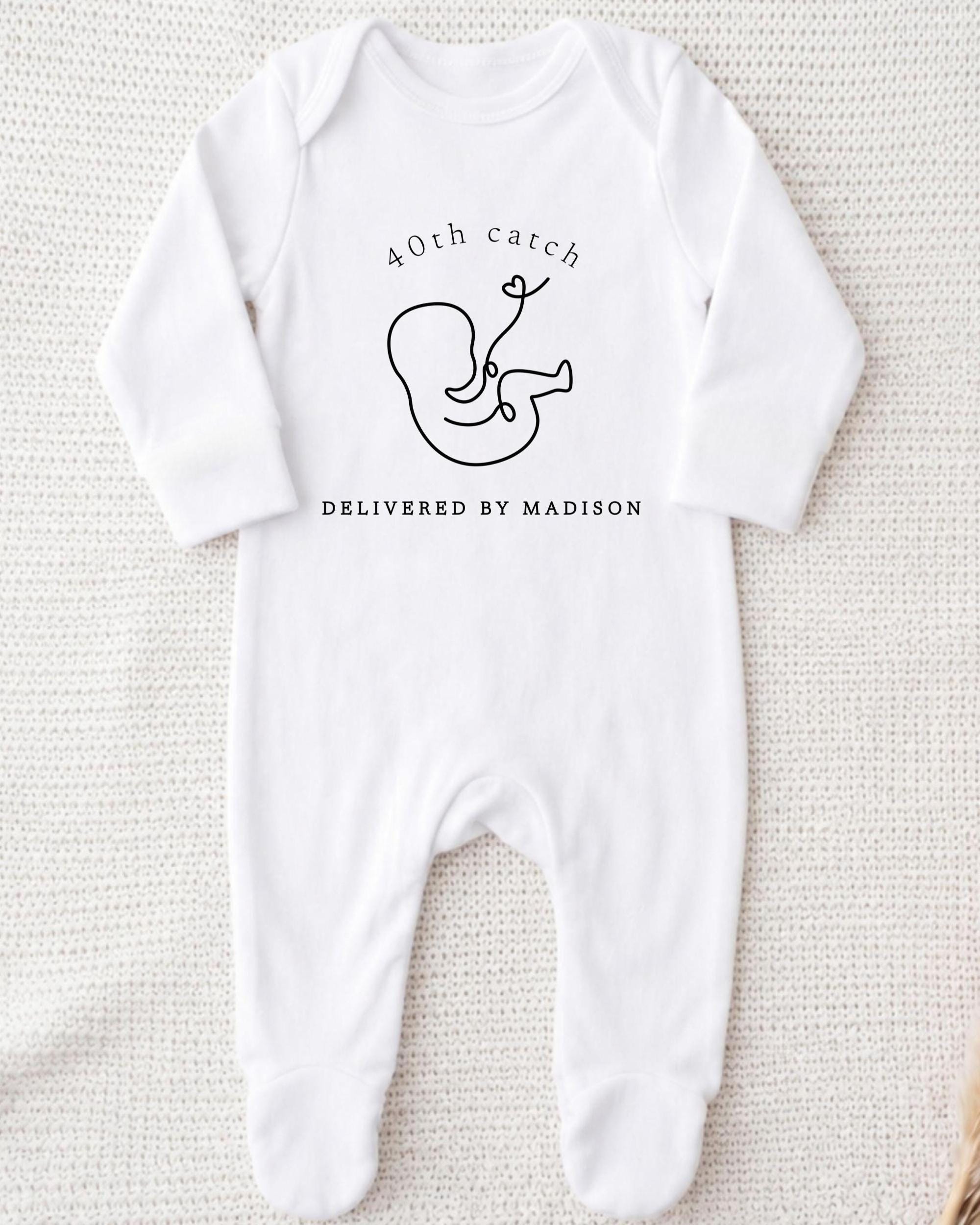A white onesie with a graphic of a baby and text that reads "40th catch DELIVERED BY MADISON".