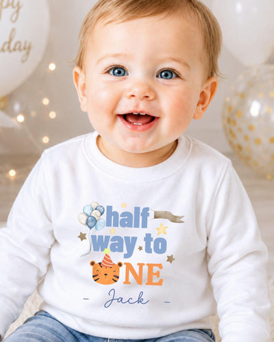 A smiling baby boy wearing a white shirt with a birthday message printed on it.