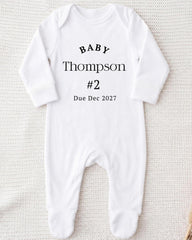 A white onesie with text printed on it, indicating the baby's name and the date of the baby's announcement.