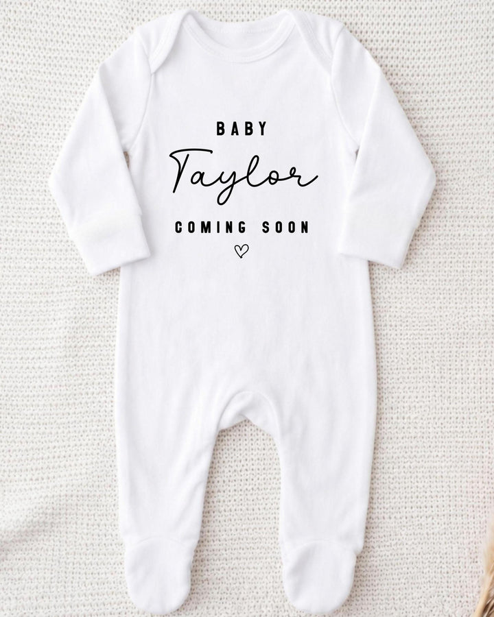 A white bodysuit with the text "BABY Taylor Coming Soon" printed on it.