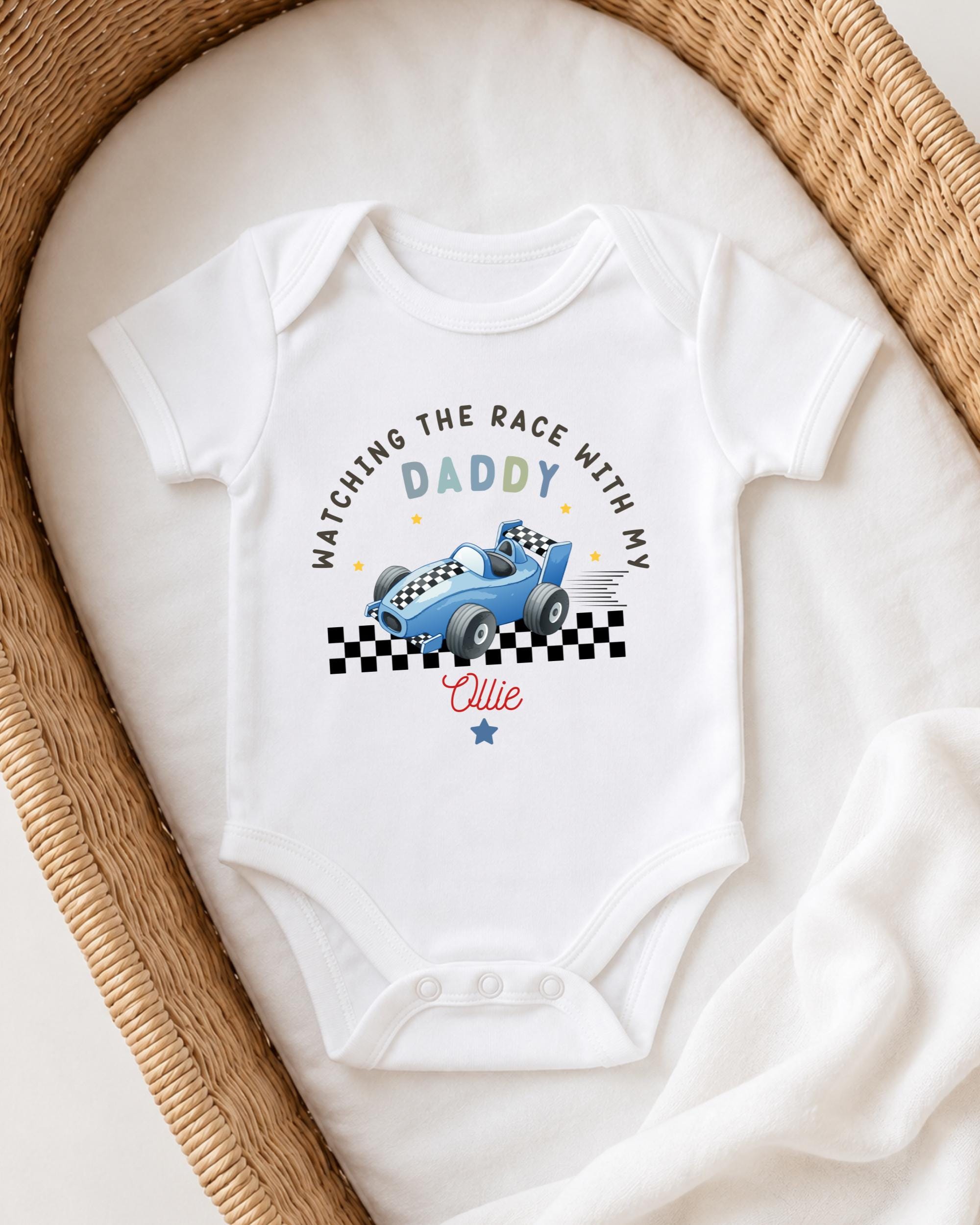 A white onesie with a racing car design and text printed on it, placed in a woven basket.