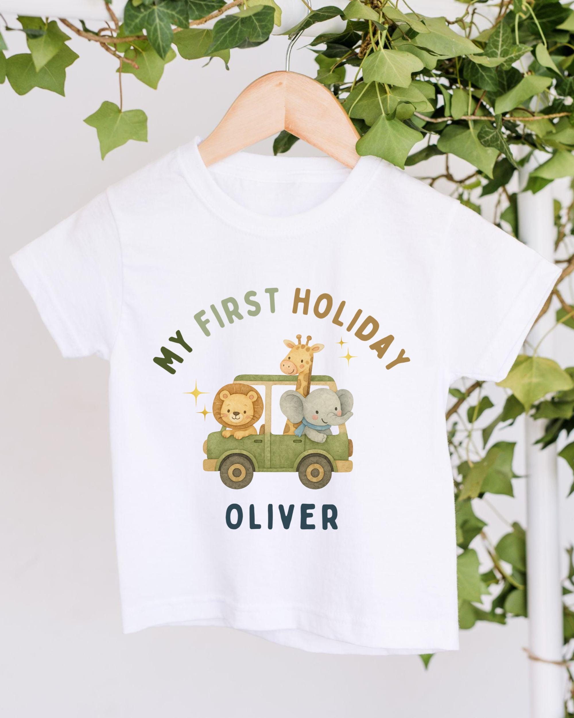 A white t-shirt with a graphic design featuring a lion, giraffe, and elephant in a safari vehicle, along with the text "My first holiday Oliver".