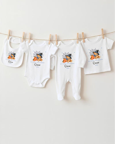A row of four white baby clothes with a spider design and the name "Oscar" printed on them, hanging on a clothesline.