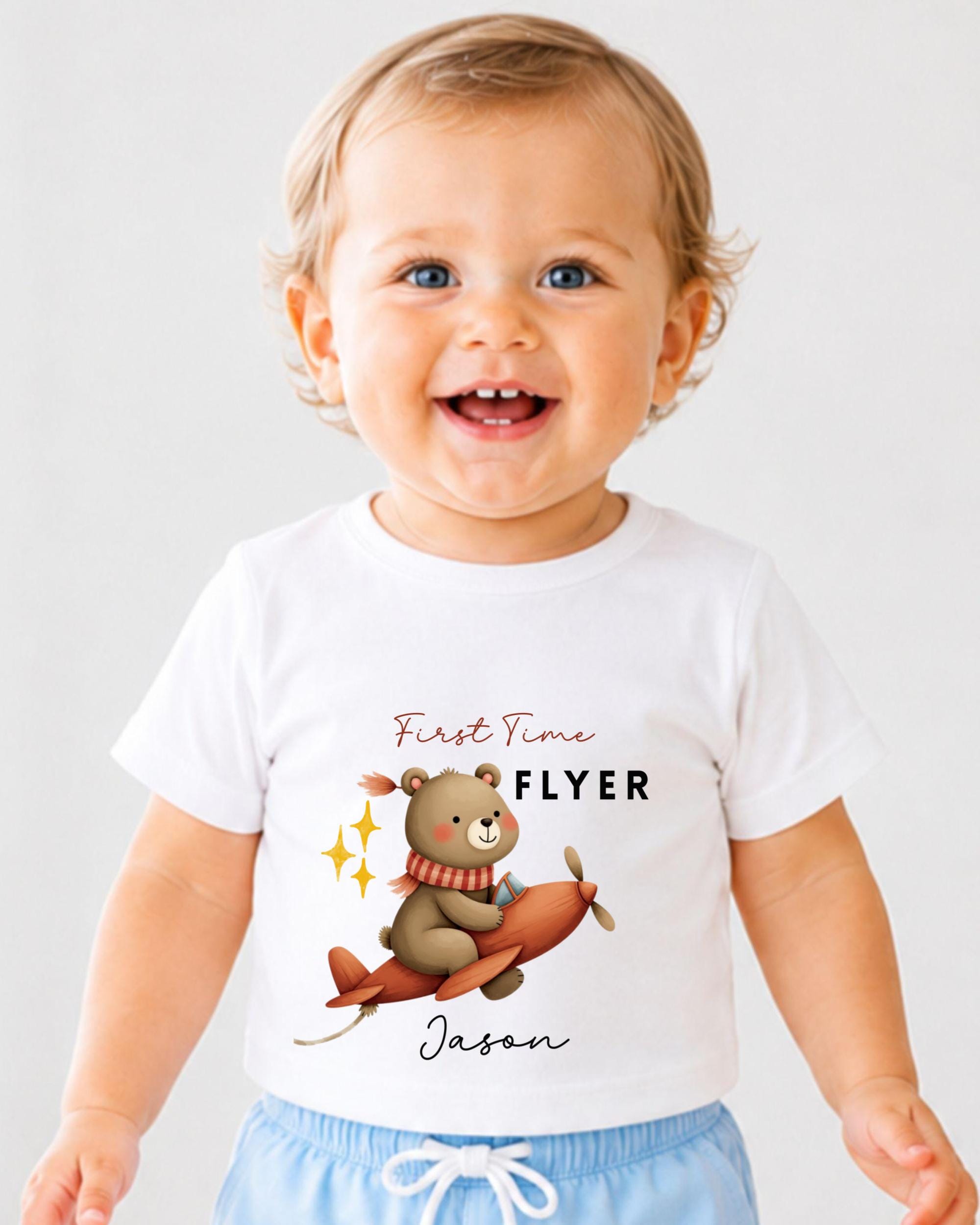 A smiling baby boy wearing a white t-shirt with a cartoon bear and airplane graphic, along with the text "First Time Flyer Jason".