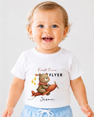 A smiling baby boy wearing a white t-shirt with a cartoon bear and airplane graphic, along with the text "First Time Flyer Jason".