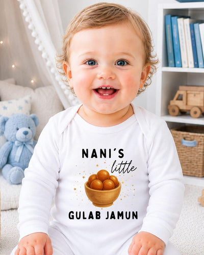 A smiling baby wearing a white onesie with a graphic and text printed on it, sitting in a room with a teddy bear and bookshelf in the background.