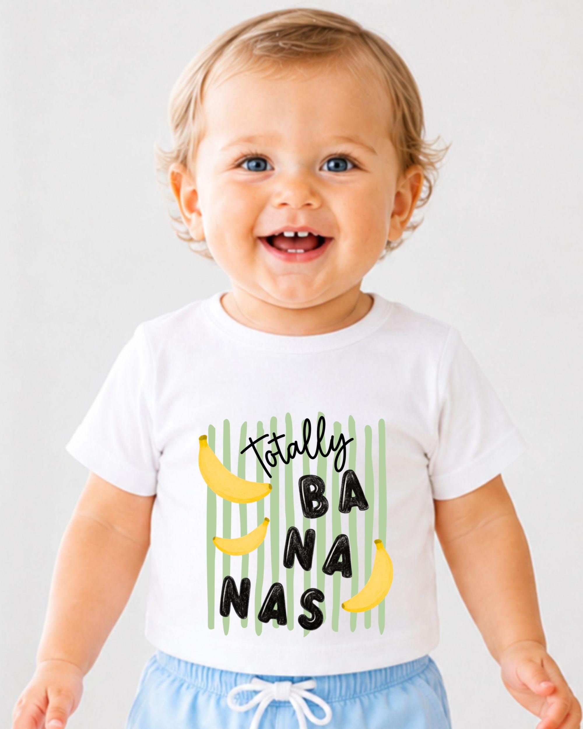 A smiling baby wearing a white t-shirt with a graphic design of bananas and the text "Totally Banana" printed on it.