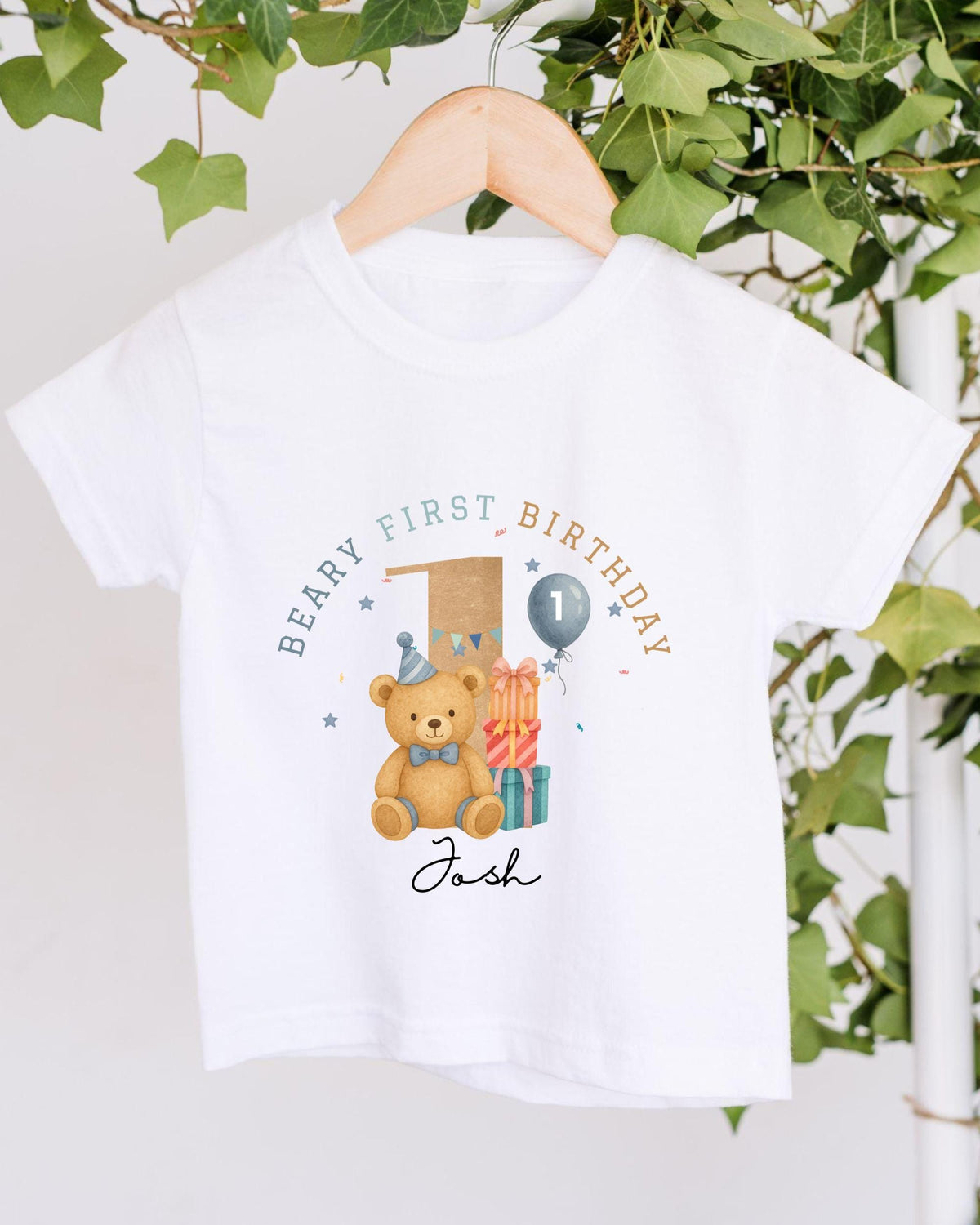 A white t-shirt with a graphic design featuring a teddy bear and a birthday balloon, along with the text "Beary First Birthday" and the name "Josh" written below.