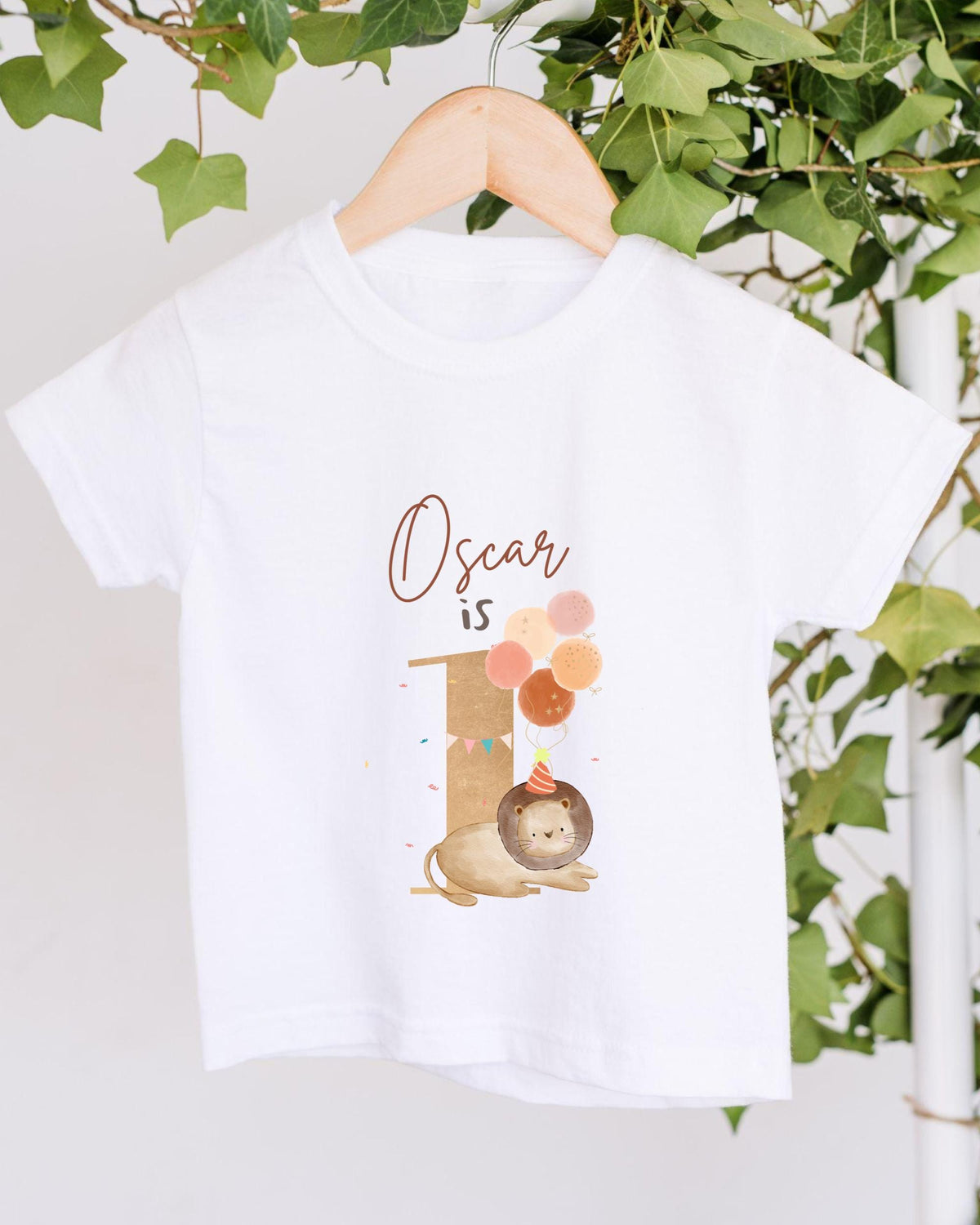 A white t-shirt with a graphic design featuring a lion and balloons, along with the text "Oscar is" printed on it.