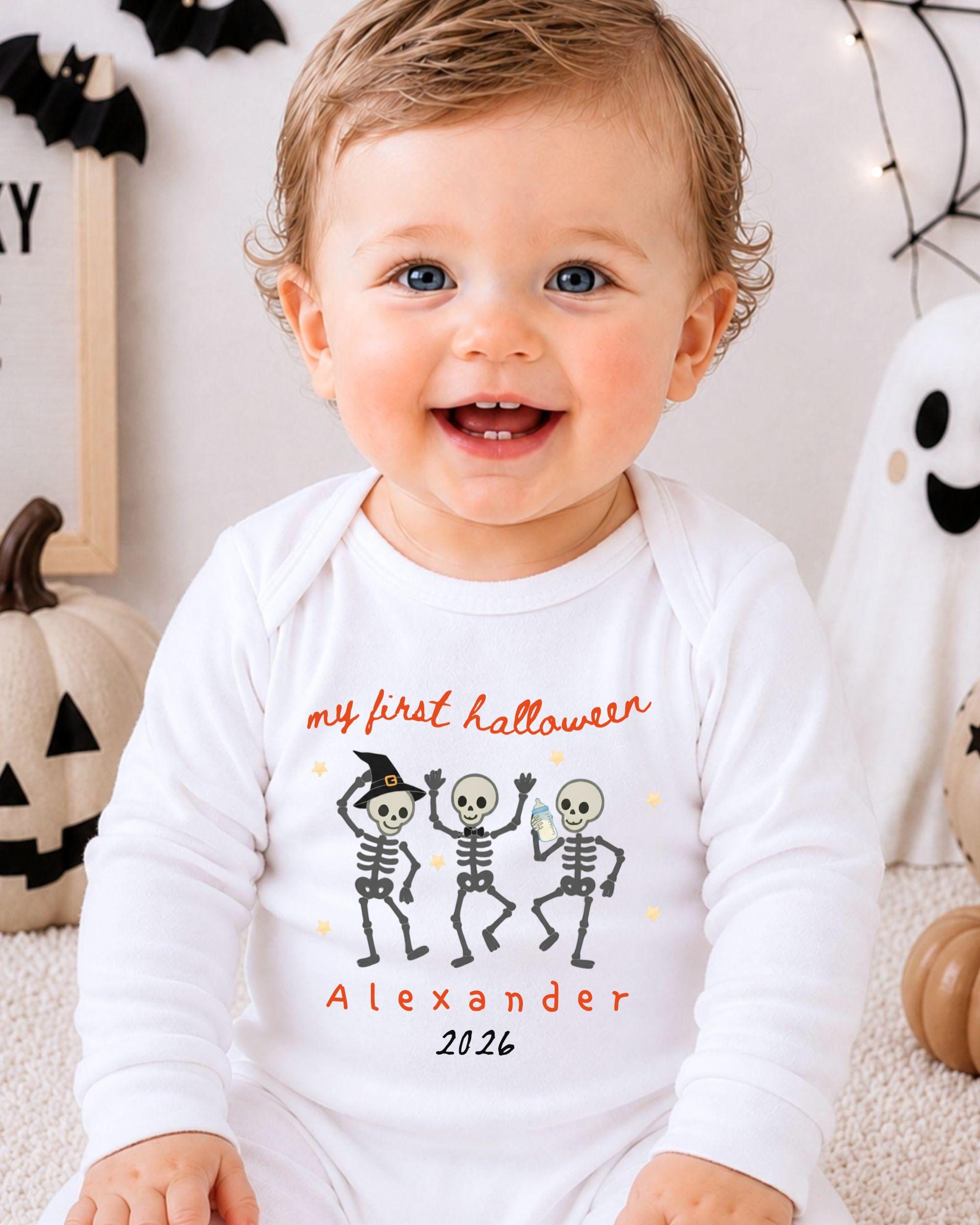 A smiling baby wearing a white onesie with a Halloween-themed design, including three cartoon skeletons and the text "my first Halloween Alexander 20.26".