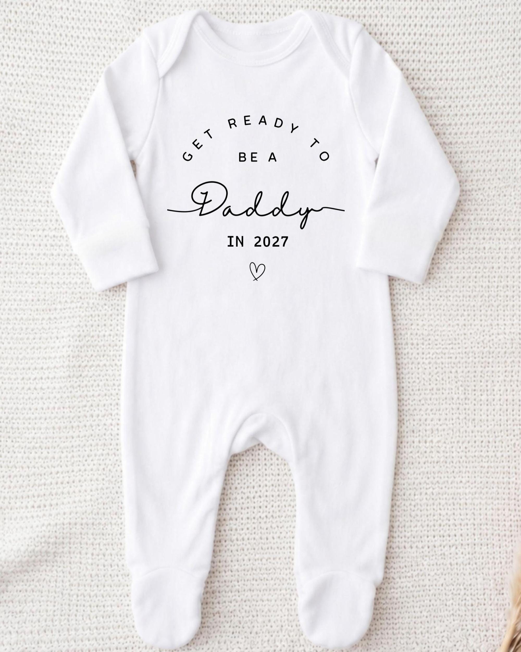 A white onesie with the text "GET READY TO BE A Daddy IN 2027" printed on it.
