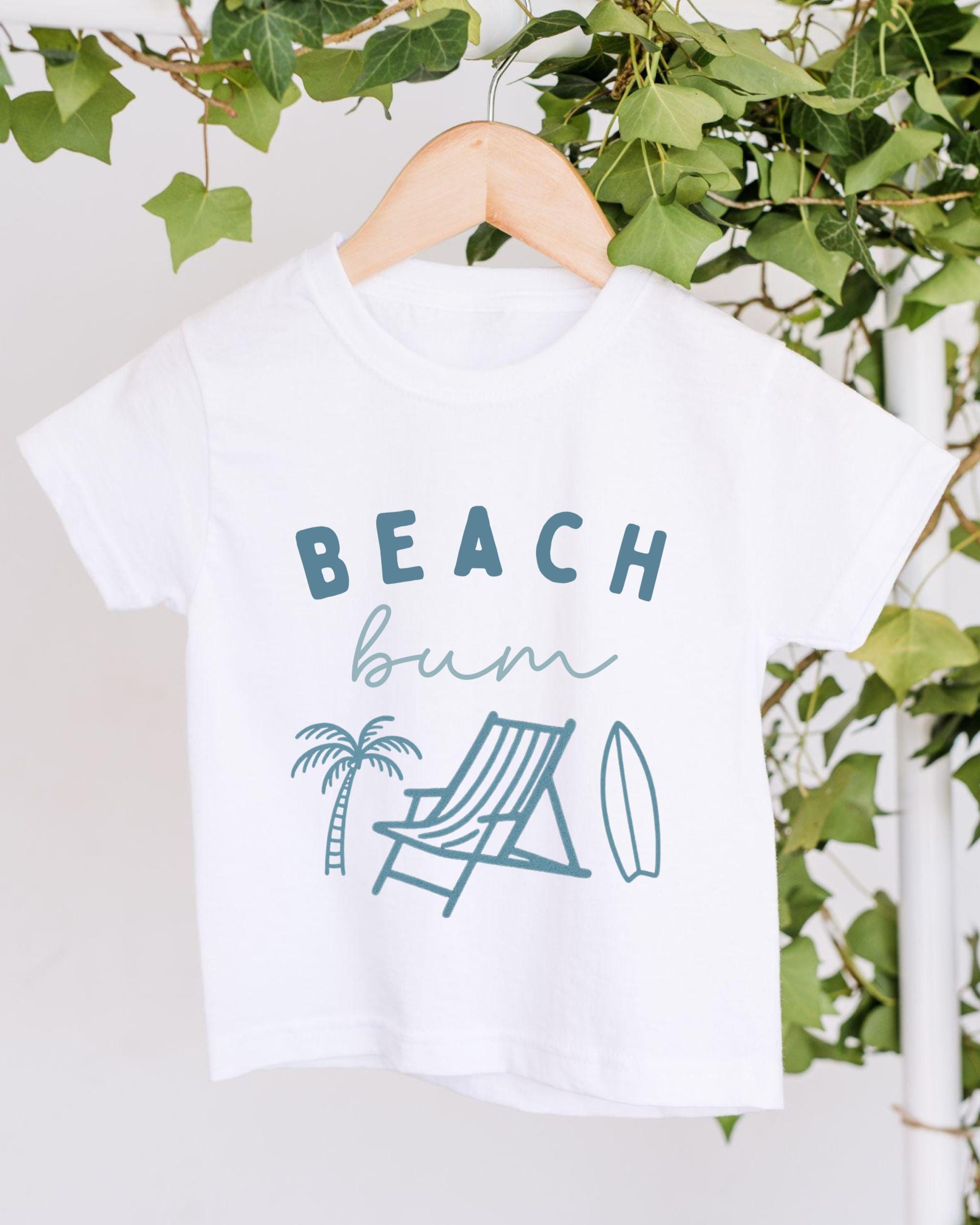 A white t-shirt with the text "BEACH butt" printed on it, along with illustrations of a beach chair, palm tree, and surfboard.