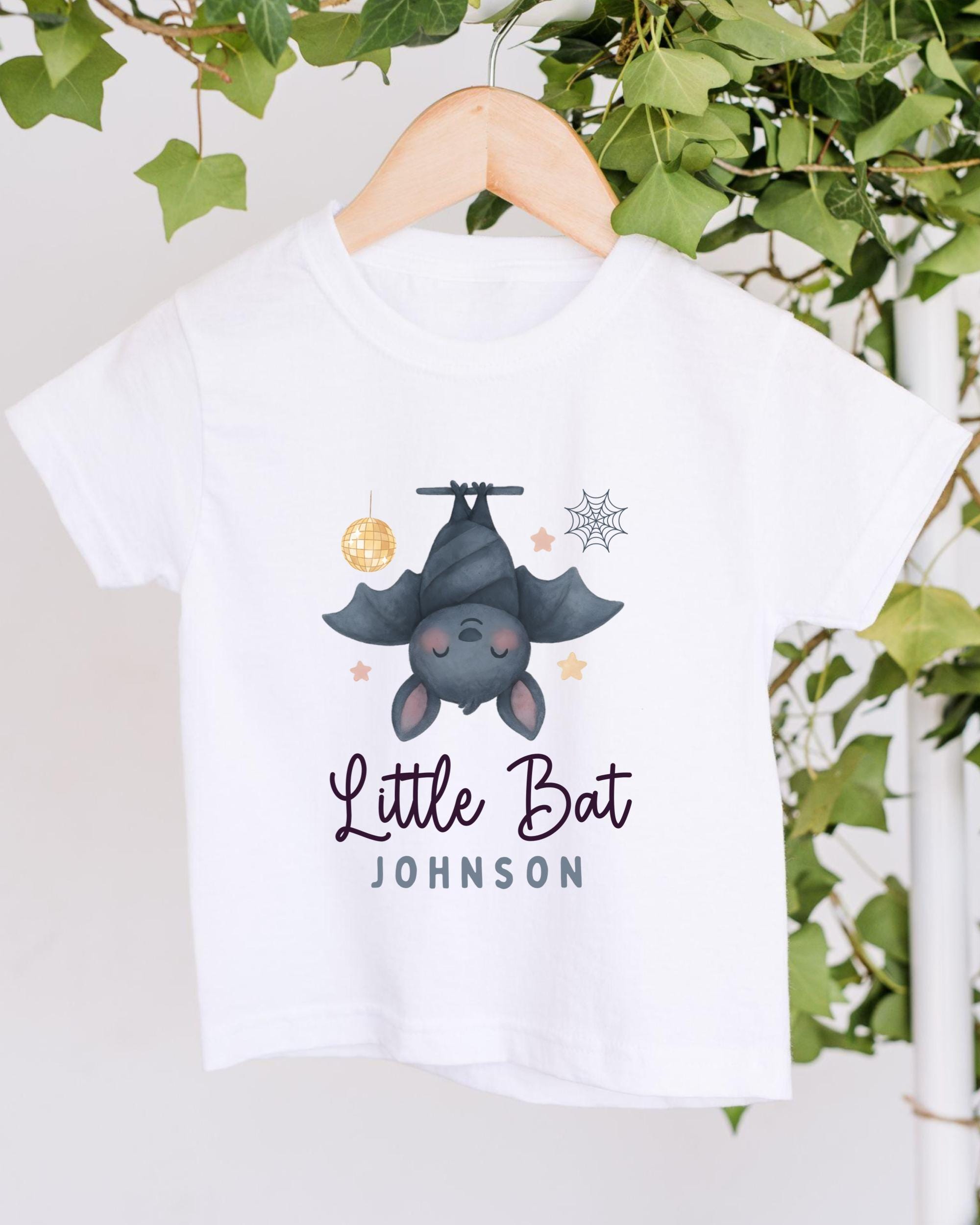 A white t-shirt with a cartoon image of a bat hanging upside down and the text "Little Bat Johnson" printed on it.