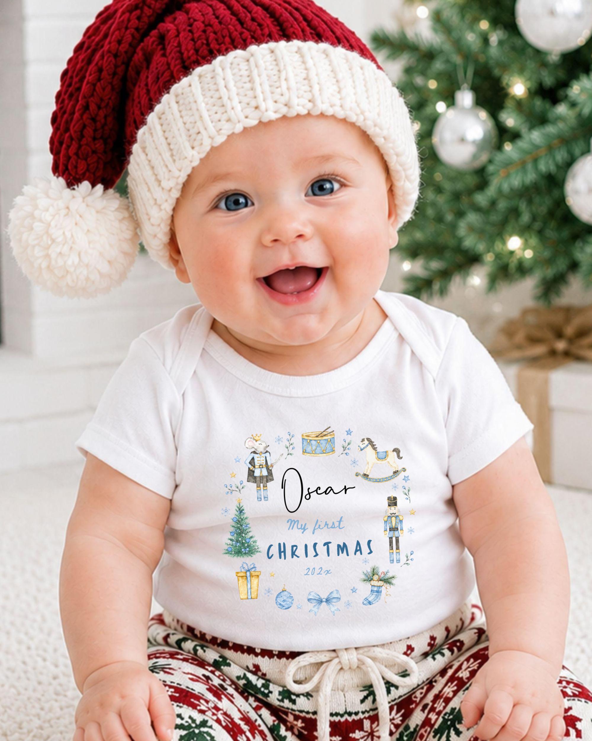 A smiling baby wearing a Santa hat and a white t-shirt with a Christmas-themed design.