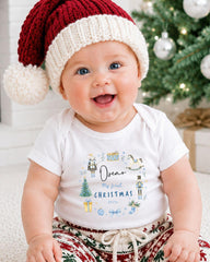 A smiling baby wearing a Santa hat and a white t-shirt with a Christmas-themed design.