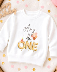 A white sweatshirt with a birthday message printed on it, surrounded by confetti.