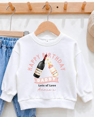 A white sweatshirt with a graphic design on it, featuring a bottle of wine and a baby bottle, along with the text "Happy Birthday Daddy Lots of Love Annex".
