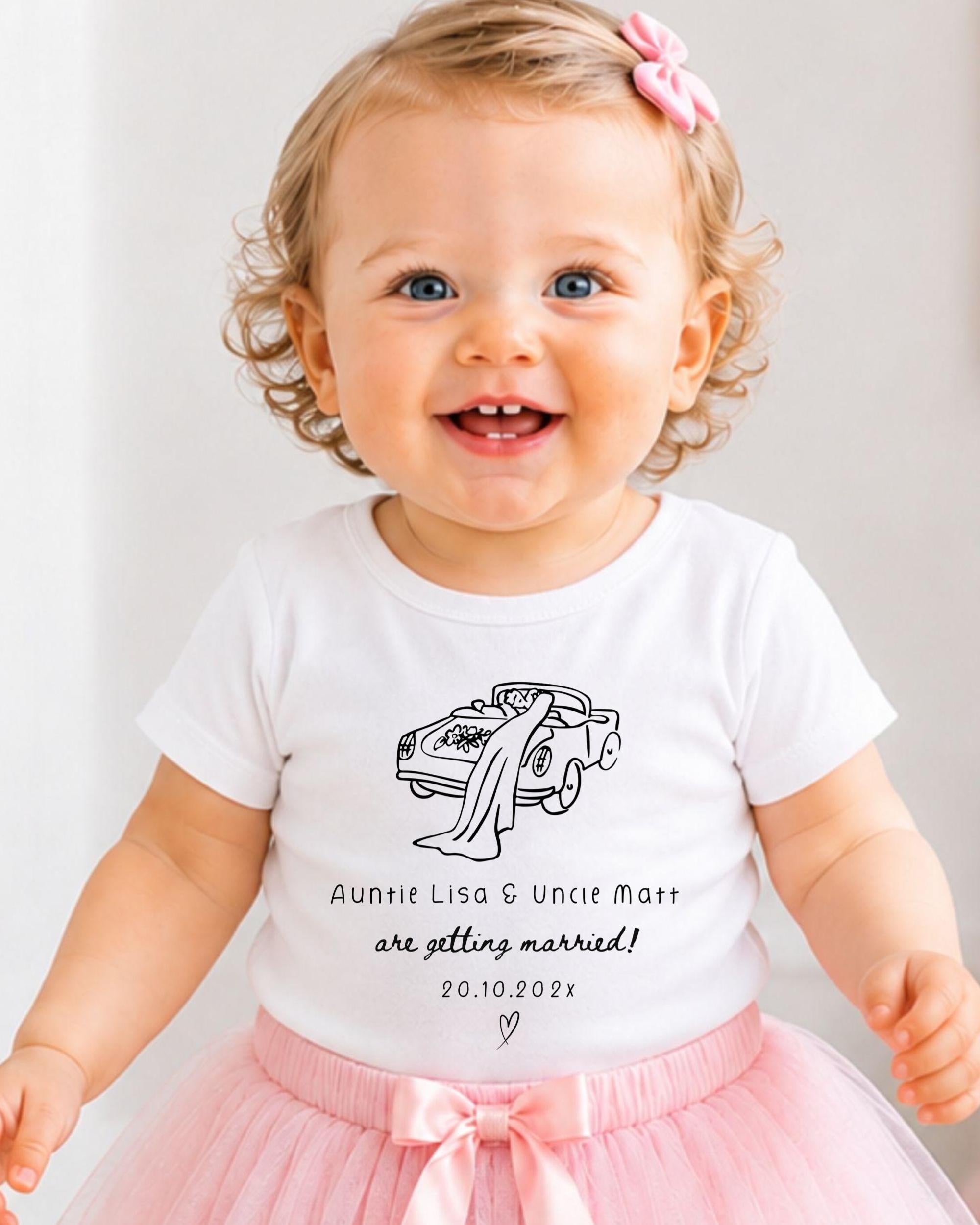 A smiling baby girl wearing a white t-shirt with a graphic of a car and text that says "Auntie Lisa & Uncle Matt are getting married! 20.10.2021".