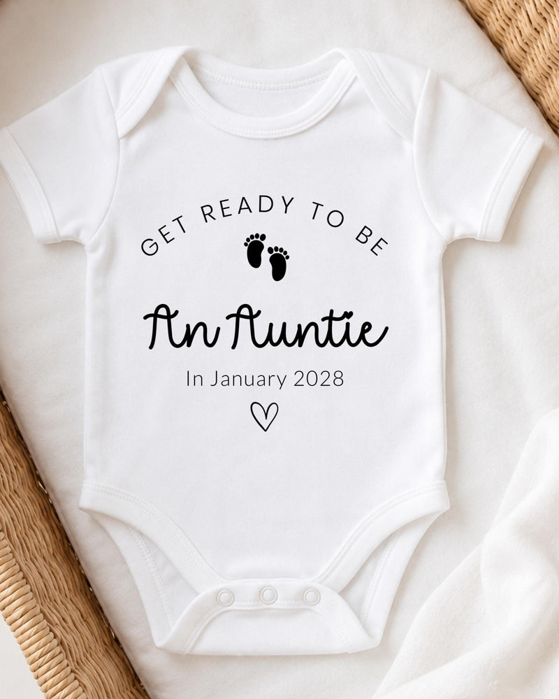A white baby bodysuit with the text "Get ready to be An Auntie" printed on it, along with a small heart symbol.