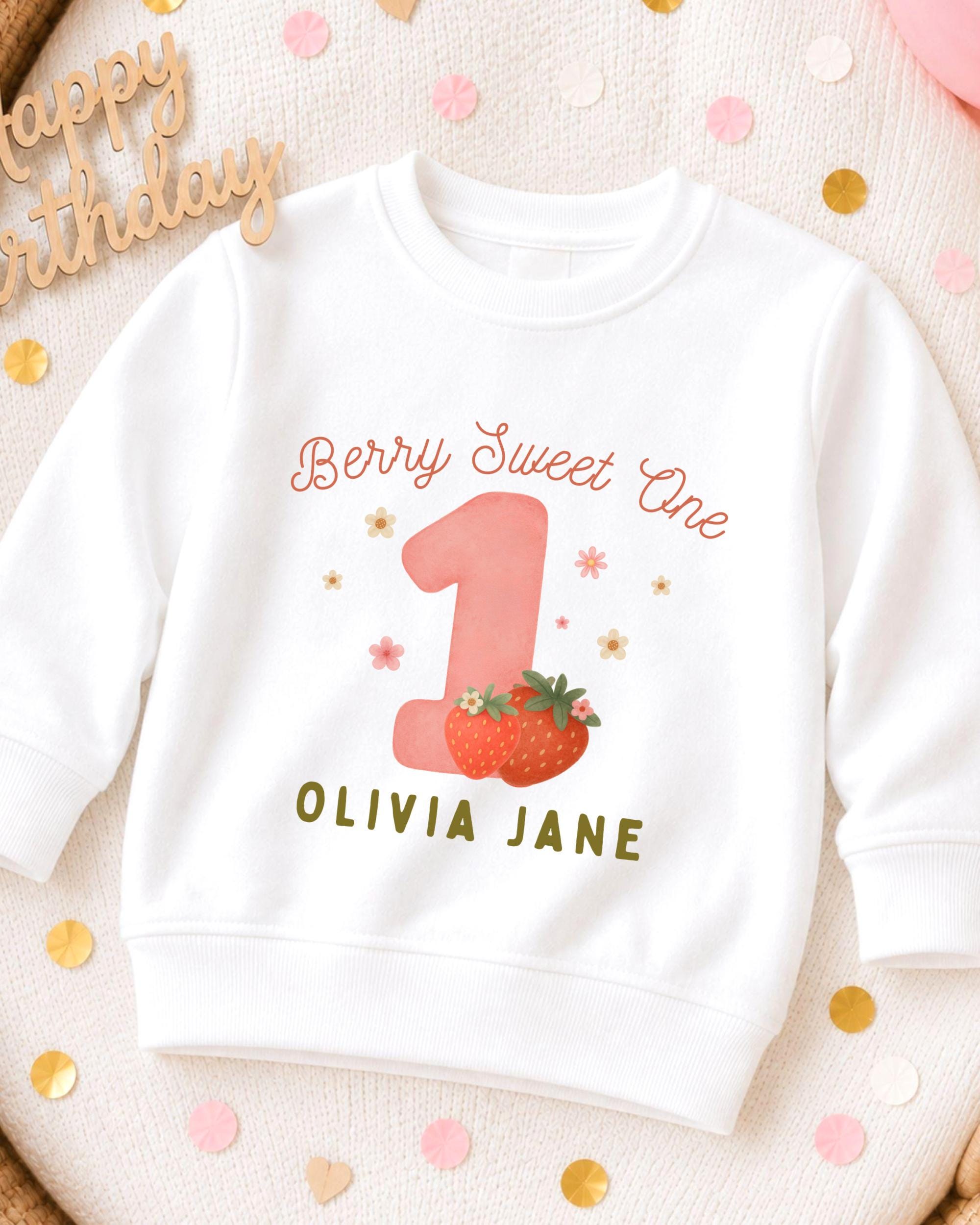 A white sweatshirt with a personalized design for a first birthday celebration.