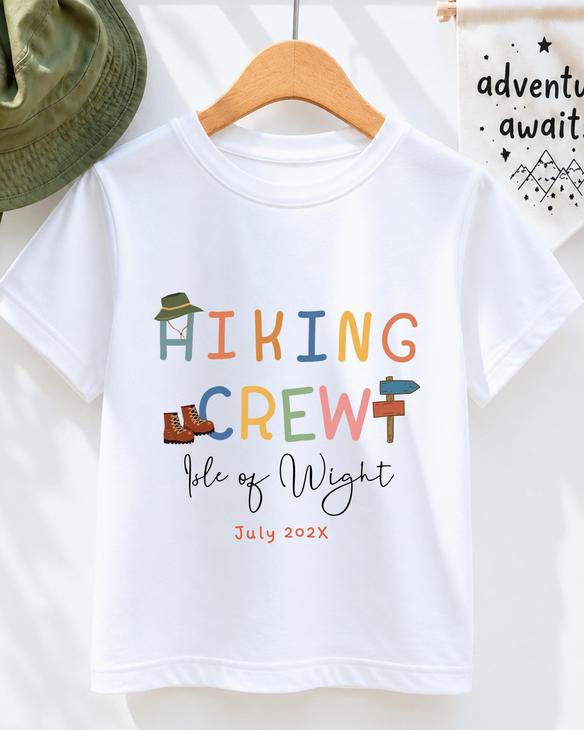 A white t-shirt with colorful text and illustrations, including the words "Hiking Crew" and " Isle of Wight" along with the date "July 2023".
